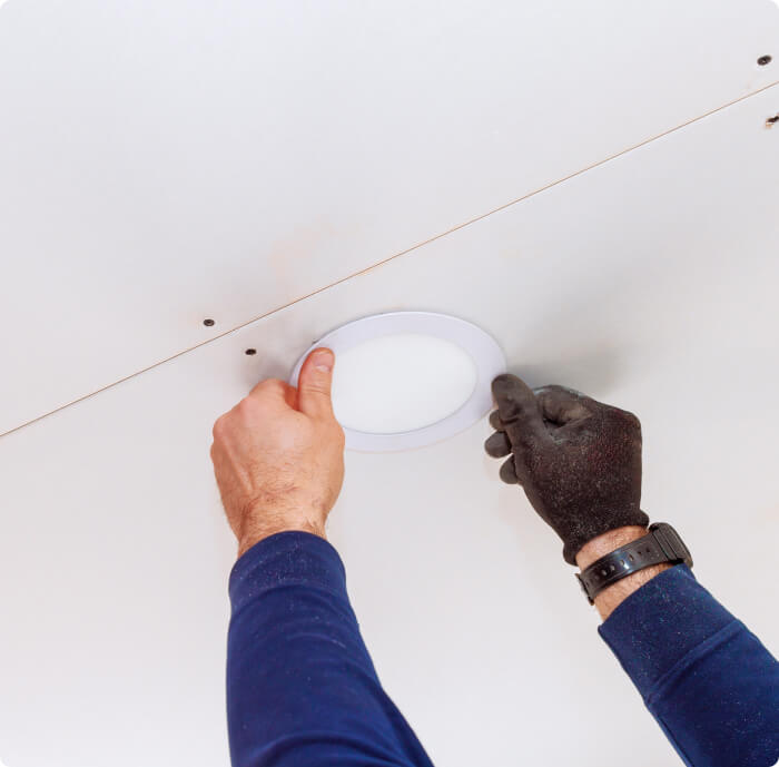 Two arms are installing a light fixture. One hand is gloved.